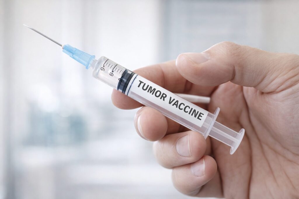 Close-up of a hand holding a syringe labeled “TUMOR VACCINE,” representing a personalized cancer mRNA vaccine, against a softly blurred clinical background.